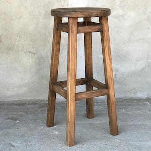 Op de afbeelding: Een houten barstoel met een bruine beitsafwerking. De stoel heeft een vierkant bovenblad en vier poten.