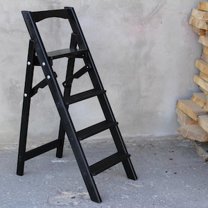 K&ouml;nnte beinhalten: Ein schwarzer Holztritt mit vier Stufen. Der Tritt ist zusammengeklappt und hat eine kleine Plattform auf der obersten Stufe.