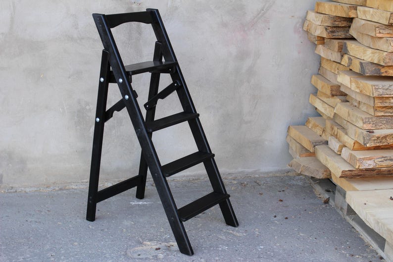 K&ouml;nnte beinhalten: Ein schwarzer Holztritt mit vier Stufen. Der Tritt ist zusammengeklappt und hat eine kleine Plattform auf der obersten Stufe.