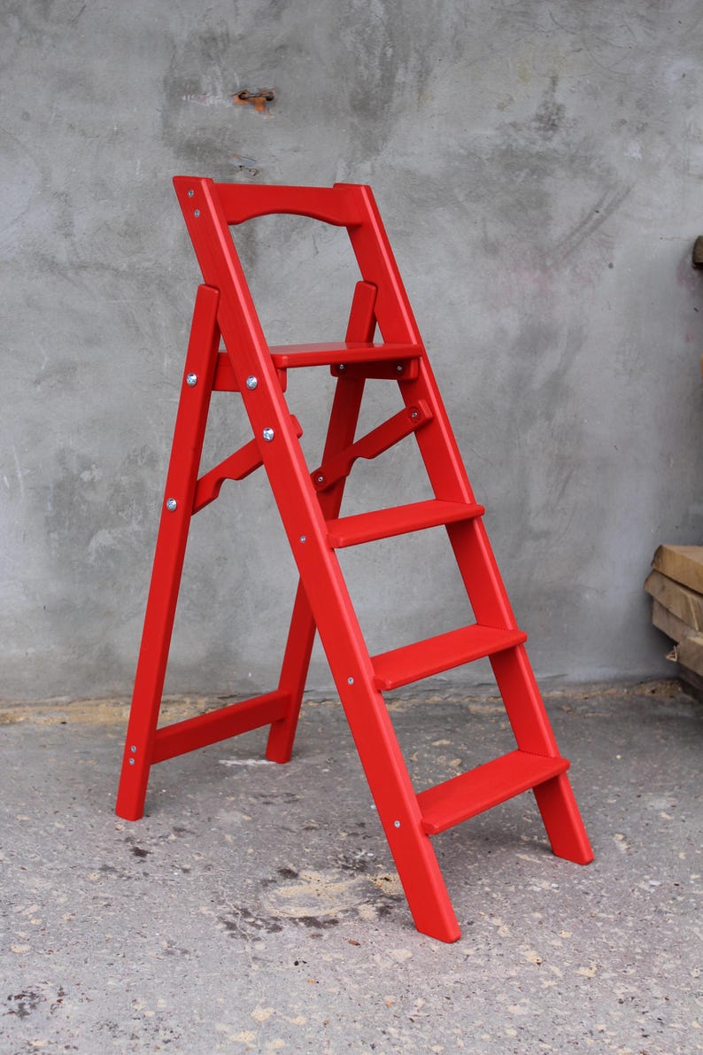 K&ouml;nnte beinhalten: Eine rote Holztreppe mit f&uuml;nf Stufen. Die Treppe ist zusammengeklappt und steht auf einer Betonfl&auml;che.