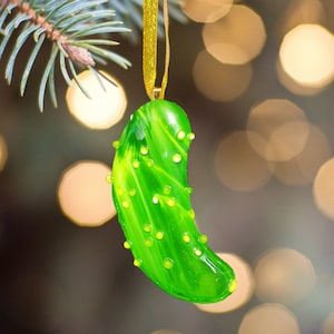 May include: A green pickle-shaped Christmas bauble with a gold string for hanging. The bauble is made of glass and has a swirl pattern.