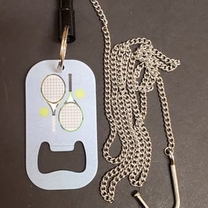 May include: A light blue bottle opener with a silver chain and a black clip. The bottle opener has a graphic of two tennis rackets and tennis balls.
