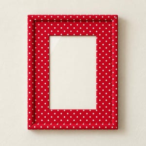 May include: A rectangular picture frame featuring a vibrant red fabric covering with a repeating pattern of small white polka dots. The frame has a thick, padded border surrounding a central rectangular opening with a clear glass pane.