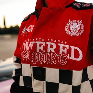 May include: Red and black racing jacket with a checkered pattern on the bottom. The jacket has a white embroidered logo that says "Lowered Empire" and "Speed Meets Luxury".