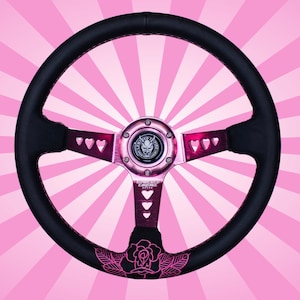 May include: Black leather steering wheel with a pink rose design and pink accents. The steering wheel has a heart-shaped cut-out design and a pink metal center cap with a logo.