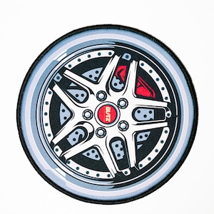 May include: A round, black and white embroidered patch with a silver car wheel design. The wheel has a red brake caliper and the word "BLITZ" in red letters.