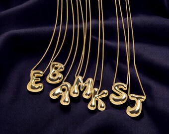 May include: A set of gold-colored necklaces with letter pendants. The letters are in a bubble font and include E, B, A, M, K, S, and J.