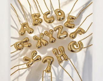 May include: A set of gold-colored necklaces with letter pendants. Each pendant is a different letter of the alphabet, and they are all in a puffy, balloon-like style.