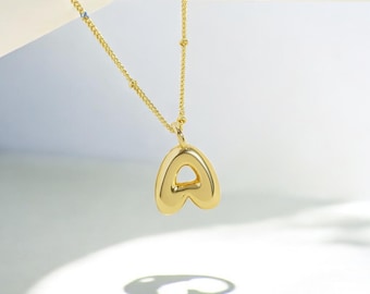 May include: A gold chain necklace with a chunky gold letter A pendant. The letter A is shaped like a heart.