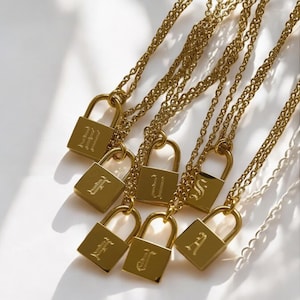 Może przedstawiać: Złote naszyjniki z kłódkami i kluczami z zawieszkami z inicjałami. Zawieszki w kształcie kłódki są grawerowane literami H, F, U, S, A i J.