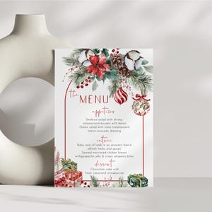 May include: A rectangular menu card featuring a red arched border and watercolor illustrations of pine branches, red poinsettias, cotton bolls, pinecones, red berries, and Christmas ornaments. The text lists appetizers, entrees, and desserts.