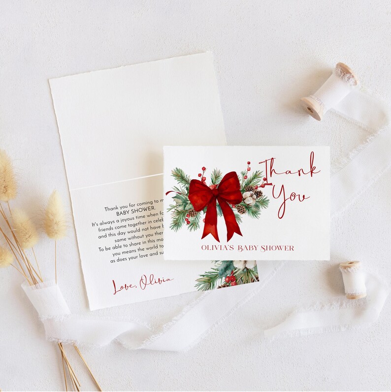 Peut inclure: Une carte de remerciement blanche pli&eacute;e pour une f&ecirc;te pr&eacute;natale avec une illustration aquarelle de branches de pin, de baies rouges et d'un grand n&oelig;ud rouge. Le texte indique Thank You et Olivia's Baby Shower en rouge avec un message imprim&eacute;.