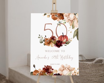 May include: A rectangular birthday welcome sign on a wooden easel featuring the number 50 in a large rose gold font, surrounded by watercolor illustrations of autumn flowers, greenery, and a pumpkin, with the text Amanda's 50th Birthday.