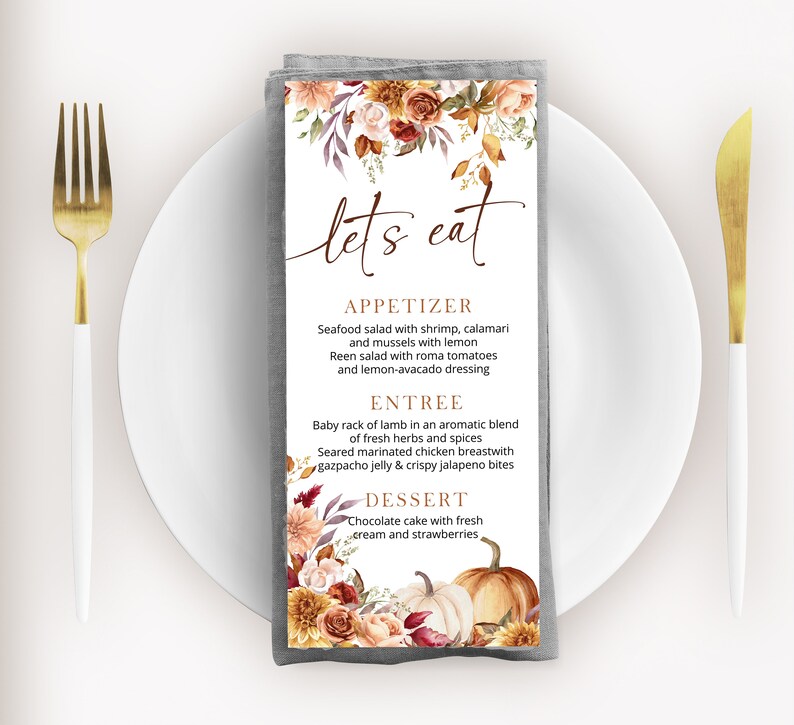May include: A gray linen napkin with a fall-themed menu printed on it. The menu features a floral design with pumpkins and the text "let's eat". The menu includes appetizers, entrees, and desserts.