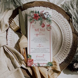 May include: A rectangular paper menu with red text and holiday illustrations of poinsettias, pine branches, and gift boxes. The menu lists sections for appetizer, entree, and dessert, featuring items like seafood salad, baby rack of lamb, and chocolate cake.