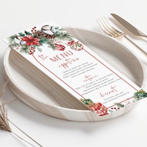 May include: A rectangular menu card featuring a watercolor illustration of poinsettias, pine cones, and ornaments. The text reads THE MENU, appetizer, entree, and dessert, with listed food items. The card is placed on a round plate with cutlery.