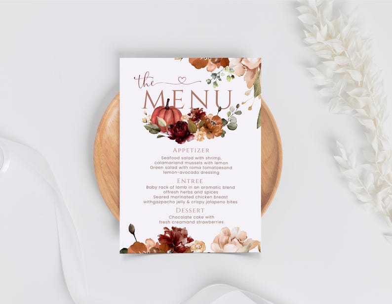 以下が含まれることがあります： 「the MENU」というセリフ体の文字が印刷された長方形のメニューカード。上部と下部にはカボチャ、濃い赤やオレンジの花、緑の葉の透明水彩画が描かれており、背景は白地となっている。