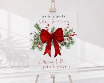 Peut inclure: Un panneau de bienvenue rectangulaire blanc sur un chevalet en bois avec un grand nœud rouge, des branches de pin vertes, des baies rouges et des pommes de pin. Le texte indique : welcome to Olivia Williams A Merry Little BABY SHOWER DEC 21. 20XX.