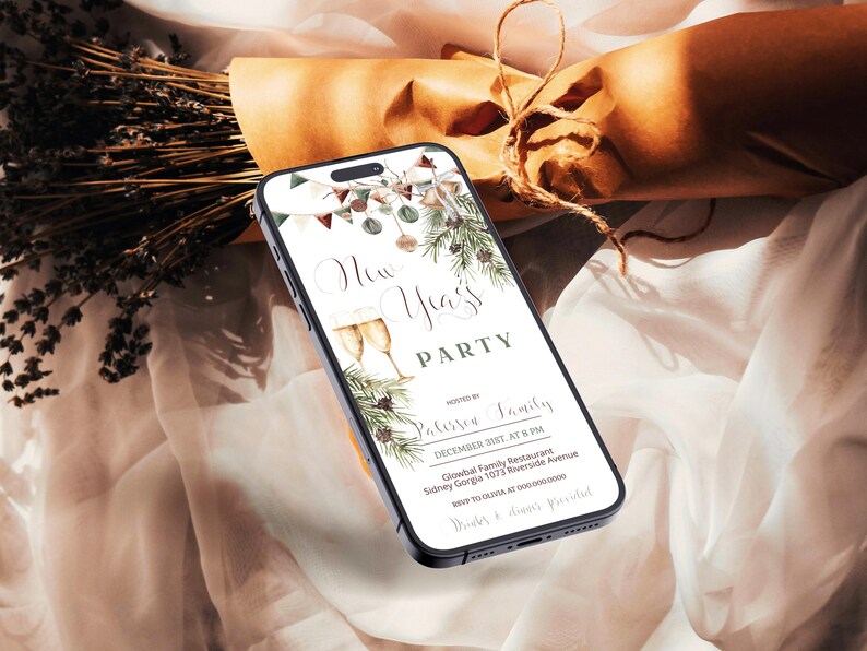 May include: A smartphone displays a New Year's Party invitation with champagne glasses and festive greenery. The phone rests on a soft, draped fabric with dried lavender and a wrapped gift in the background.
