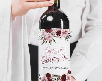 Może przedstawiać: Butelka wina z białą etykietą, na której widnieje napis "Cheers to Celebrating You" i "Happy Birthday Amanda!" Etykieta ma kwiatowy wzór z różowymi i bordowymi kwiatami.