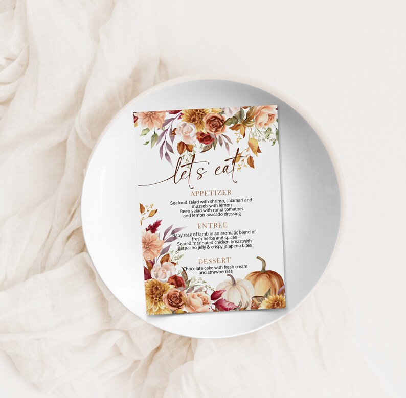 May include: A printable wedding menu card with a fall theme. The card features a watercolor illustration of autumn leaves, flowers, and pumpkins. The menu includes appetizers, entrees, and desserts. The text on the card reads "Let's Eat".