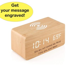 May include: A wooden digital clock with a white wireless charging pad on top. The clock displays the time 10:14 and the temperature 69 degrees Fahrenheit. The clock also has a personalized message engraved on the front: "You are not running late Mom! I love you, xoxo Jason."
