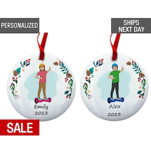 May include: Two personalized Christmas ornaments featuring a boy and a girl riding hoverboards. The ornaments are white with a green and red floral design. The boy's ornament says "Alex 2023" and the girl's ornament says "Emily 2023".