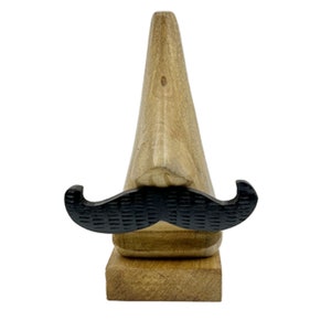 May include: Wooden figurine of a nose with a black mustache. The nose is carved from wood and has a natural wood finish. The mustache is made of black plastic and is attached to the nose.