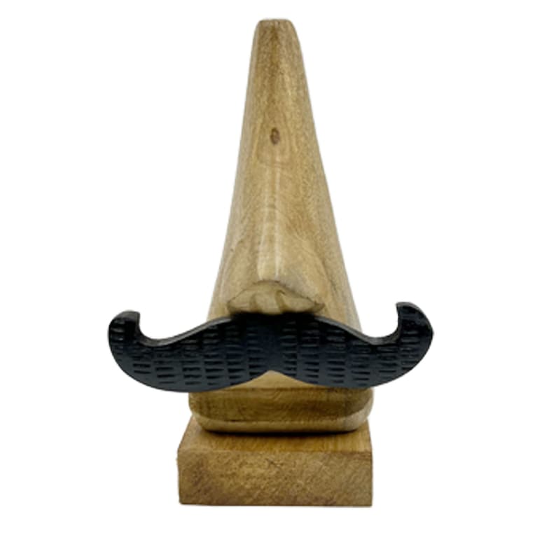May include: Wooden figurine of a nose with a black mustache. The nose is carved from wood and has a natural wood finish. The mustache is made of black plastic and is attached to the nose.