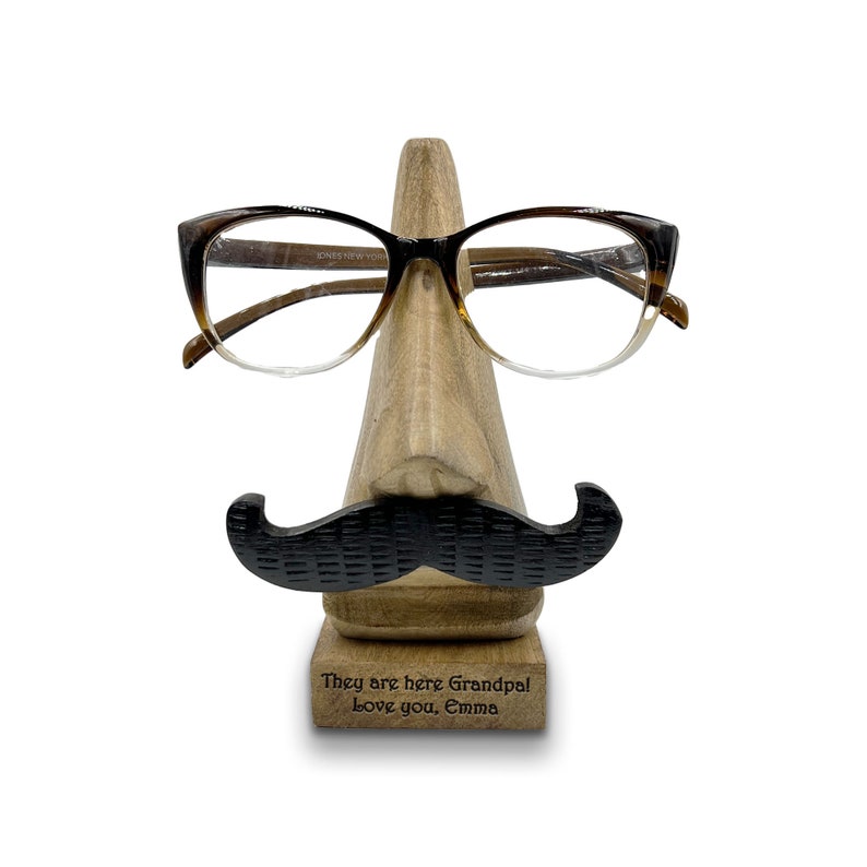 May include: Wooden eyeglasses holder shaped like a face with a mustache and glasses. The base of the holder has the text "They are here Grandpal Love you, Emma" engraved on it.