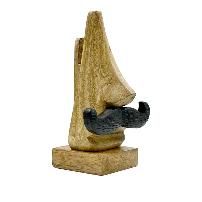 May include: Wooden stand shaped like a nose with a black mustache. The stand is made of light brown wood and has a square base.