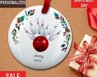 May include: White round ornament with a red bowling ball and pins design. The ornament has a red ribbon for hanging and is personalized with the name "Jerry" and the year "2021". Decorative floral elements surround the bowling scene.