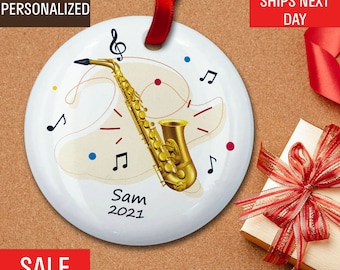 May include: A white ceramic ornament with a gold saxophone, musical notes, and the text "Sam 2021".