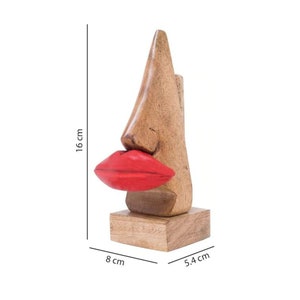 May include: Wooden sculpture of a nose with red lips, standing on a wooden base. The sculpture is 16 inches tall, 8 inches wide, and 5.4 inches deep.
