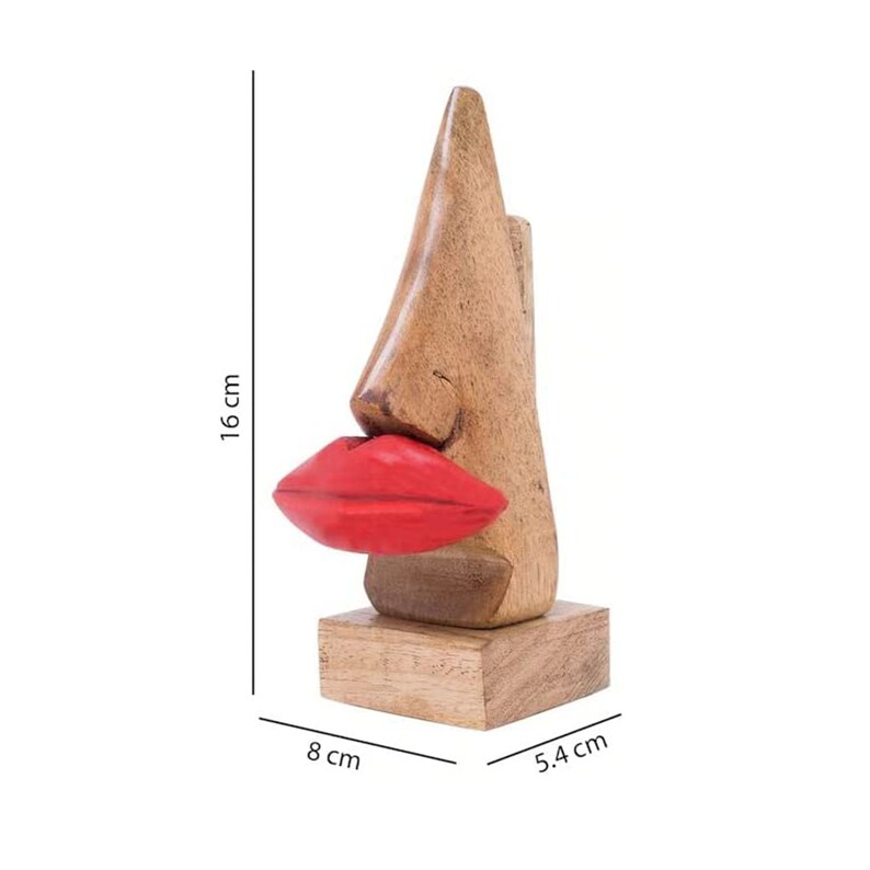 May include: Wooden sculpture of a nose with red lips, standing on a wooden base. The sculpture is 16 inches tall, 8 inches wide, and 5.4 inches deep.