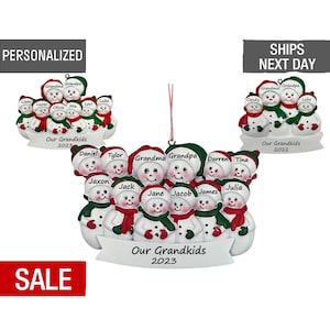 May include: A white snowman ornament with 10 snowmen, each with a different name. The snowmen are arranged in a circle with a banner that reads "Our Grandkids 2023".