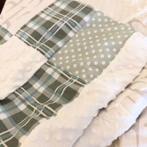 Könnte beinhalten: Eine Babydecke mit Patchwork-Design, bestehend aus einem grün-blauen Karomuster, weißen Punkten auf grauem Hintergrund und einem weißen Minky-Stoffrand. Die Decke hat ein strukturiertes, bauschiges Design.