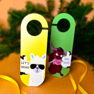 May include: Two door hangers with funny illustrations. The yellow door hanger features a llama wearing sunglasses with the text "Let's Hang". The green door hanger features a red bull with the text "Bad Idea!"