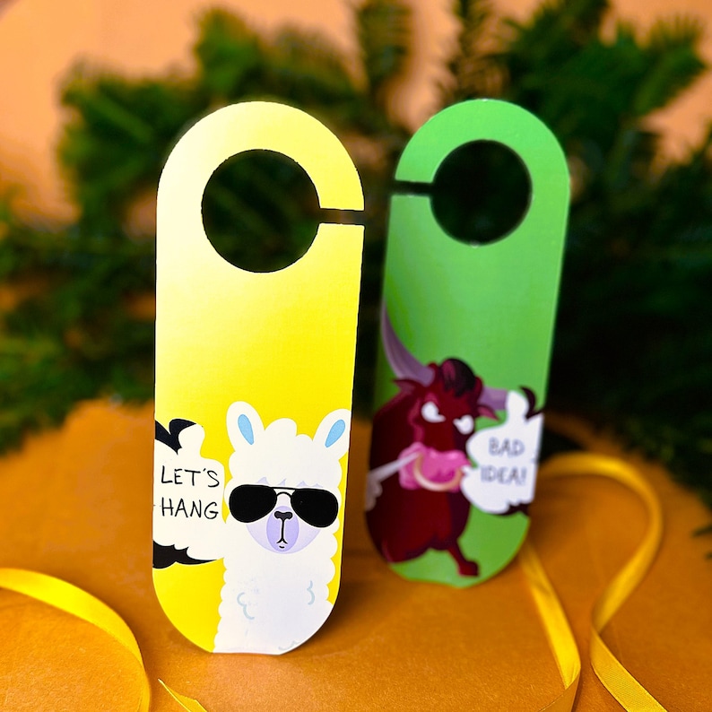May include: Two door hangers with funny illustrations. The yellow door hanger features a llama wearing sunglasses with the text "Let's Hang". The green door hanger features a red bull with the text "Bad Idea!"