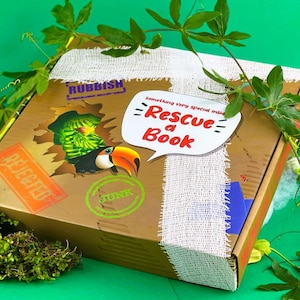 May include: A brown cardboard box with a white fabric ribbon and a toucan peeking out of a hole. The box has a green stamp that says "JUNK" and a red stamp that says "REJECTED". The box has a white speech bubble that says "something very special inside - Rescue a Book".