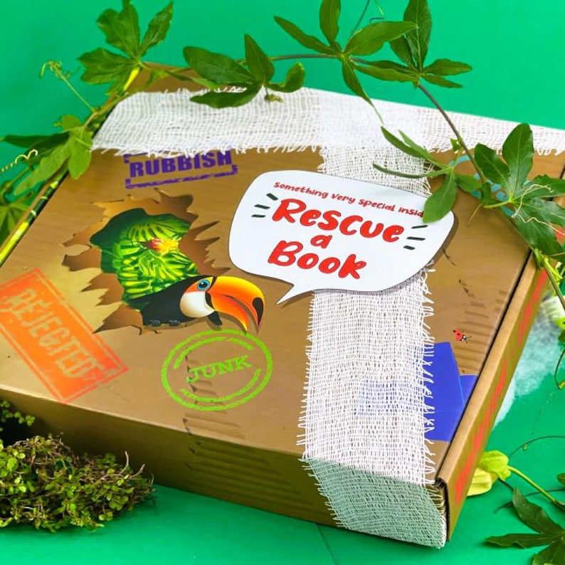 May include: A brown cardboard box with a white fabric ribbon and a toucan peeking out of a hole. The box has a green stamp that says "JUNK" and a red stamp that says "REJECTED". The box has a white speech bubble that says "something very special inside - Rescue a Book".