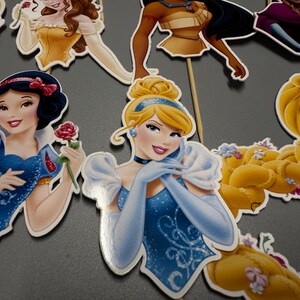 May include: A set of 10 princess character cake toppers. The toppers feature Cinderella, Snow White, Belle, Rapunzel, and Pocahontas. The toppers are made of cardboard and have a stick on the back for easy insertion into cakes.