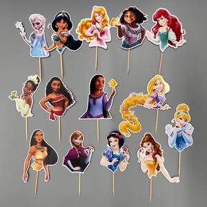 May include: A set of 13 princess themed cake toppers. The toppers feature various Disney princesses, including Cinderella, Snow White, Ariel, Belle, and more. Each topper is printed on cardstock and attached to a wooden stick.