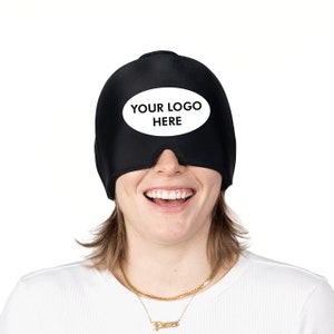 Op de afbeelding: Een persoon draagt ​​een zwart slaapmasker met een witte ovaal waarop "YOUR LOGO HERE" staat.