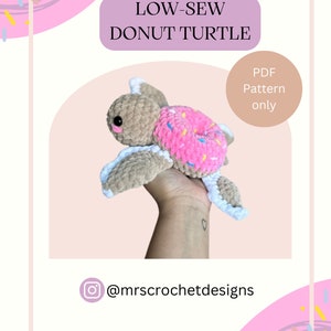 Pode incluir: Um brinquedo amigurumi de tartaruga de donut de crochê com uma casca de donut rosa e um corpo marrom. O brinquedo está sendo segurado em uma mão. A imagem inclui o texto "LOW-SEW DONUT TURTLE" e "PDF Pattern only".