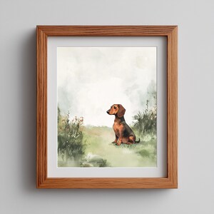May include: A framed art print featuring a watercolor illustration of a dachshund dog sitting in a grassy field. The dog is brown and black, with a focused gaze. The artwork is set in a wooden frame, with a soft, natural color palette.