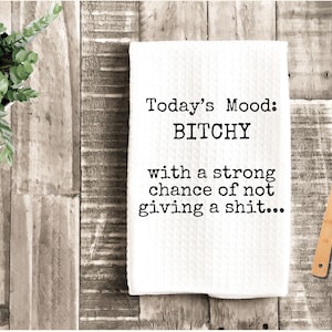 May include: White kitchen towel with the text "Today's Mood: BITCHY with a strong chance of not giving a shit...". A wooden spoon and a potted plant are also in the image.