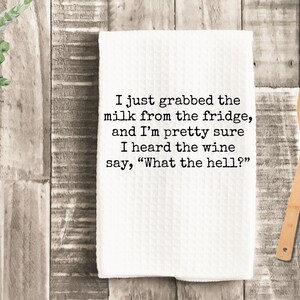 May include: White kitchen towel with black text that reads "I just grabbed the milk from the fridge, and I'm pretty sure I heard the wine say, "What the hell?""