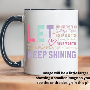 May include: White ceramic mug with a black handle. The mug has a colorful design that says "Let them keep shining" and includes the text "Misunderstand, Judge You, Gossip About You, Never Doubt Your Worth, Your Beauty".
