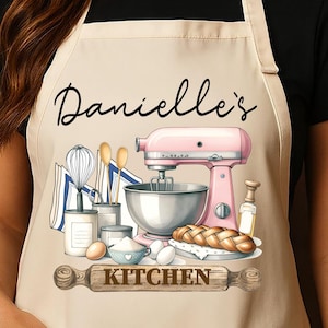 May include: Beige apron with a kitchen-themed design. The apron features the text "Danielle's" in cursive, along with illustrations of a pink stand mixer, baking tools, and the word "KITCHEN".